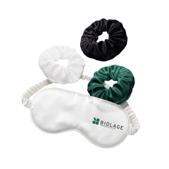 A white sleeping mask and three different coloured hair scrunchies on a white background.