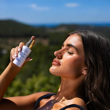 Woman applying skincare product outdoors with scenic background