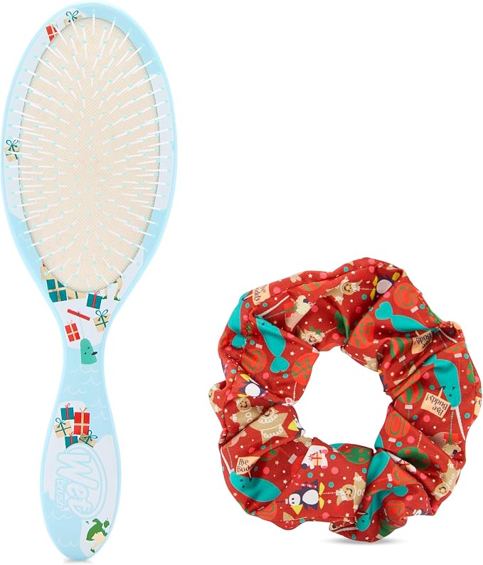 A light blue hairbrush with a Christmas-themed printed handle next to a red fabric scrunchie featuring a holiday print of penguins, snow globes, and ornaments, on a white background.