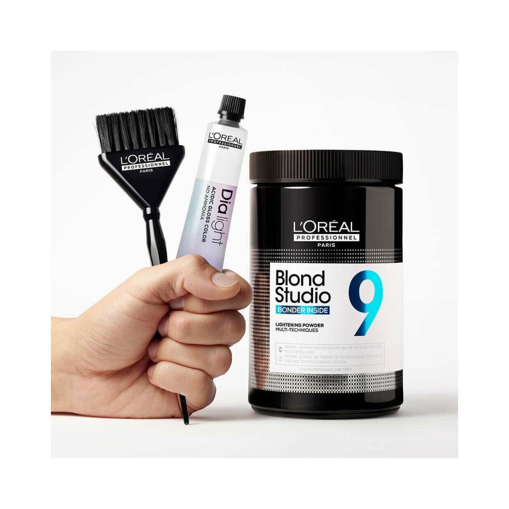 A bond Studio tube next to a hand holding a hair dye tube and a tinting brush. 