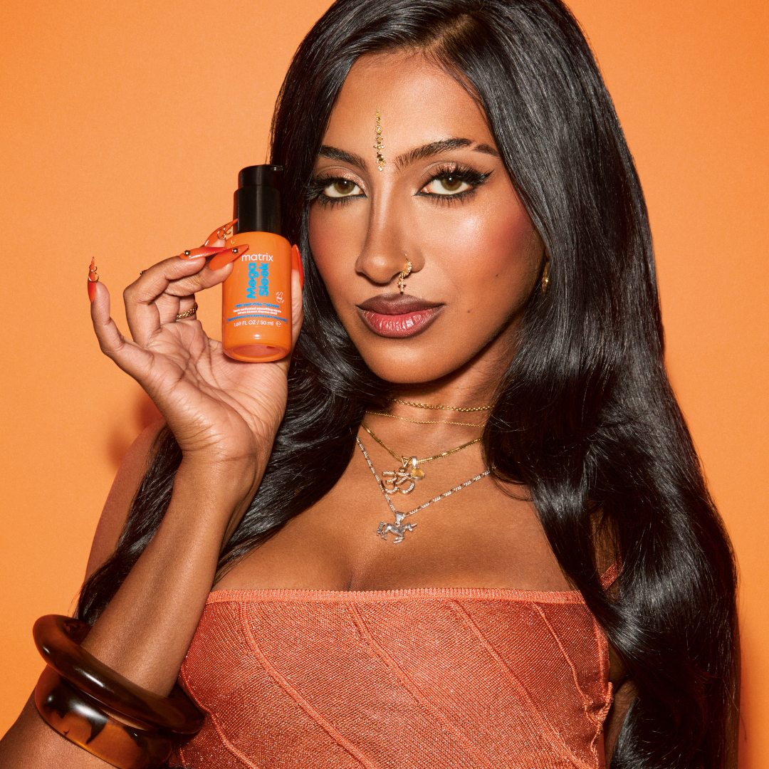 A woman with long black hair holds up an orange bottle of Nutra Body Butter against a solid orange background.