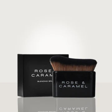 A Rose & Caramel blending brush with black bristles and a black handle, shown in front of its matching black packaging box on a light gray reflective surface.