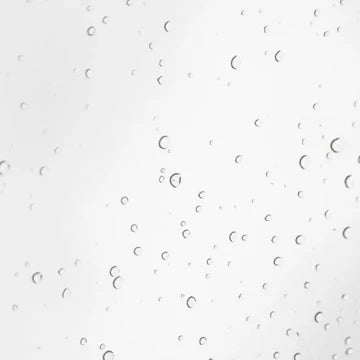 A close-up of a clear liquid with numerous small, scattered water droplets on a light gray-white background.