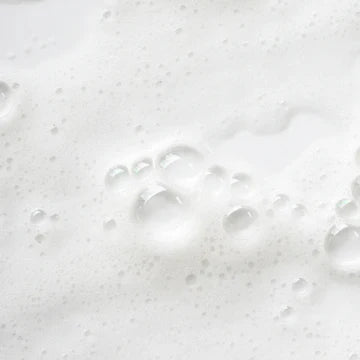 A close-up texture shot of white lathered foam with clear bubbles on a white surface.