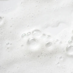 A close-up texture shot of white lathered foam with clear bubbles on a white surface.
